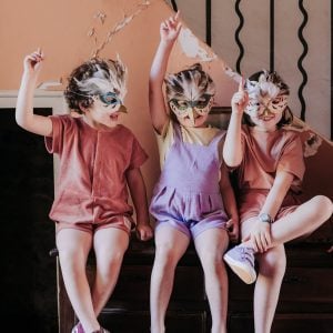 Trio d'enfants assis sur un meuble portant des masques oiseaux et habillés en Marmaï Patterns