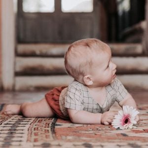 Bébé à plat ventre avec une fleur dans la main habillé en barboteuse Marmaï Patterns